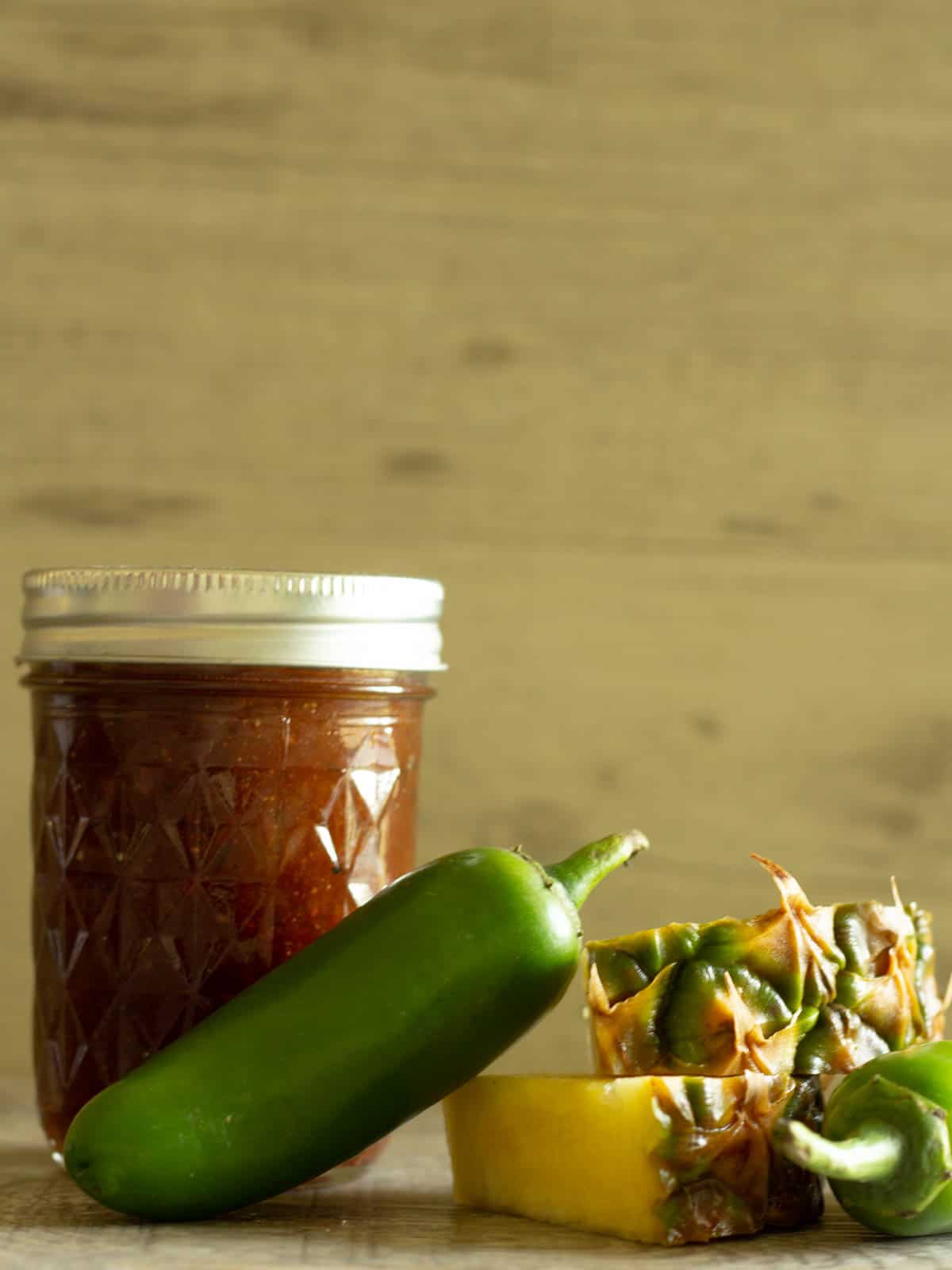 Jar of pineapple barbeque sauce next to jalapenos and fresh pineapple