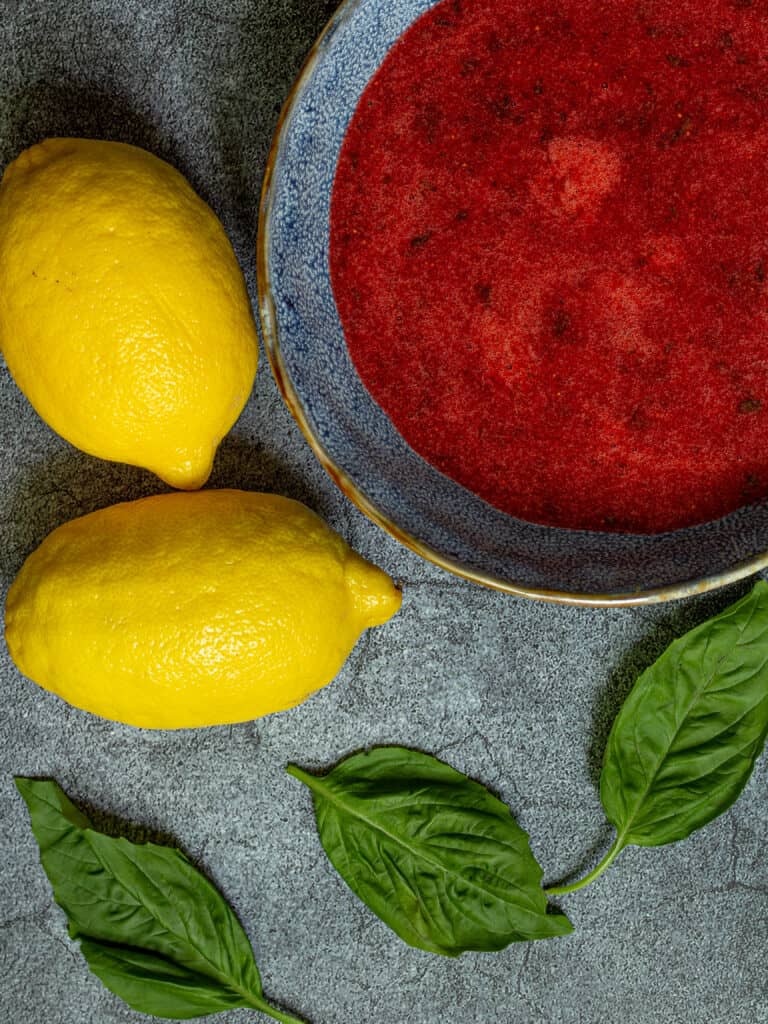 bowl of strawberry puree with lemons and basil leaves