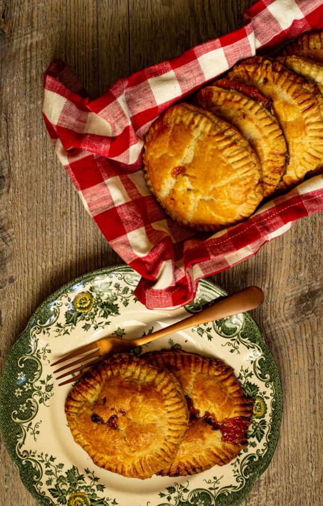 Hand pies on a plate next to hand pies in a dish wrapped in a red and white checked towel