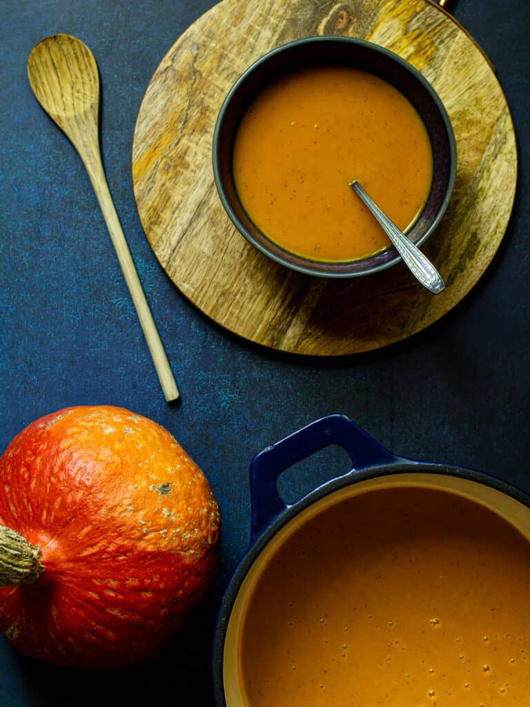 pot of red kuri squash soup with a wooden spoon and bowl of soup