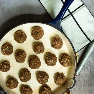 meatballs in a large skillet with a dish towel and spoon