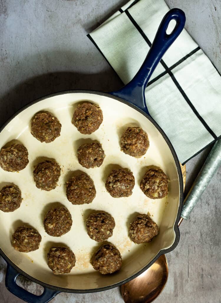 meatballs in a large skillet with a dish towel and spoon