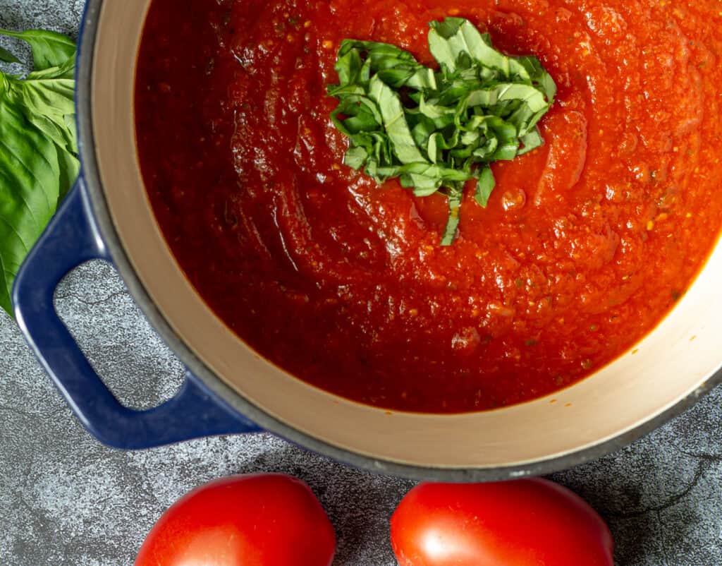 Marinara sauce in a blue pot topped with chopped basil