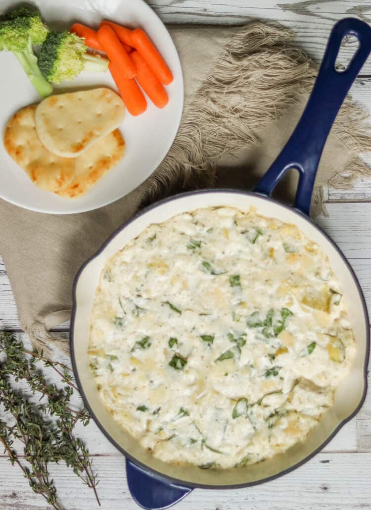 Artichoke spinach dip in a skillet with vegetables and bread