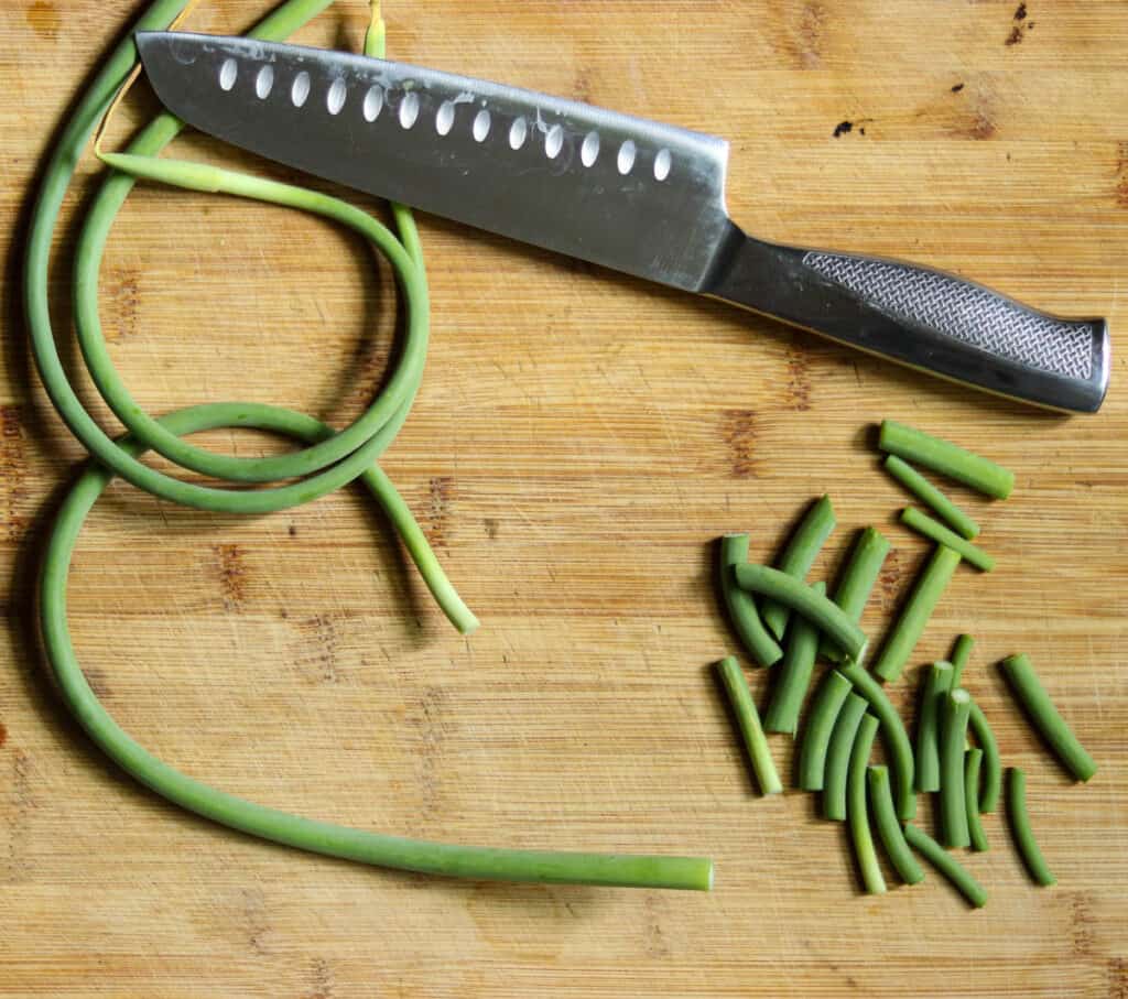 chopped garlic scapes and a knife on a cutting board