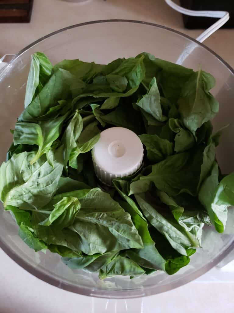 adding the basil to the food processor.