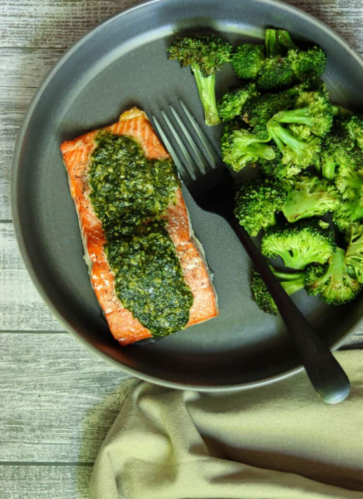 salmon with pesto butter and broccoli on a dark gray plate.