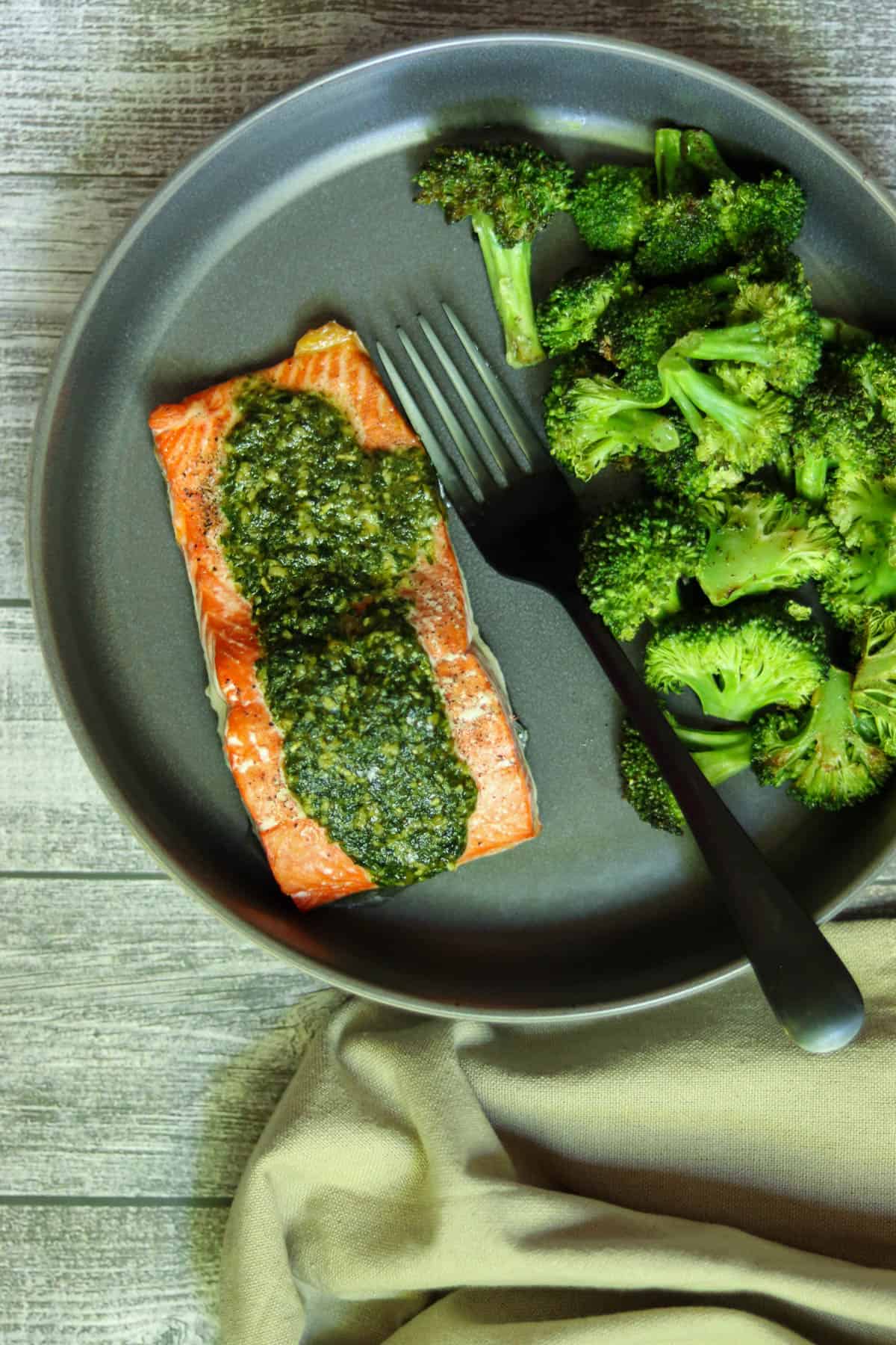 salmon with pesto butter and broccoli on a dark gray plate.