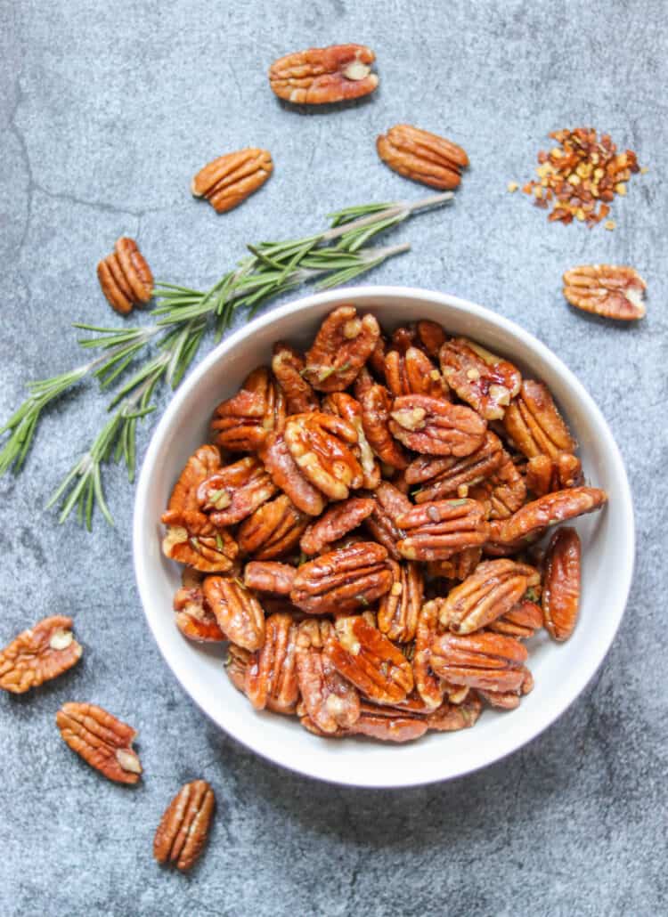 candied pecans in a bowl with fresh rosemary and red pepper flake