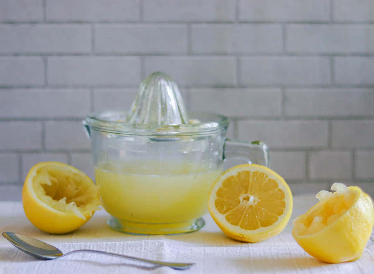 Cut Meyer lemons next to a cup of lemon juice.