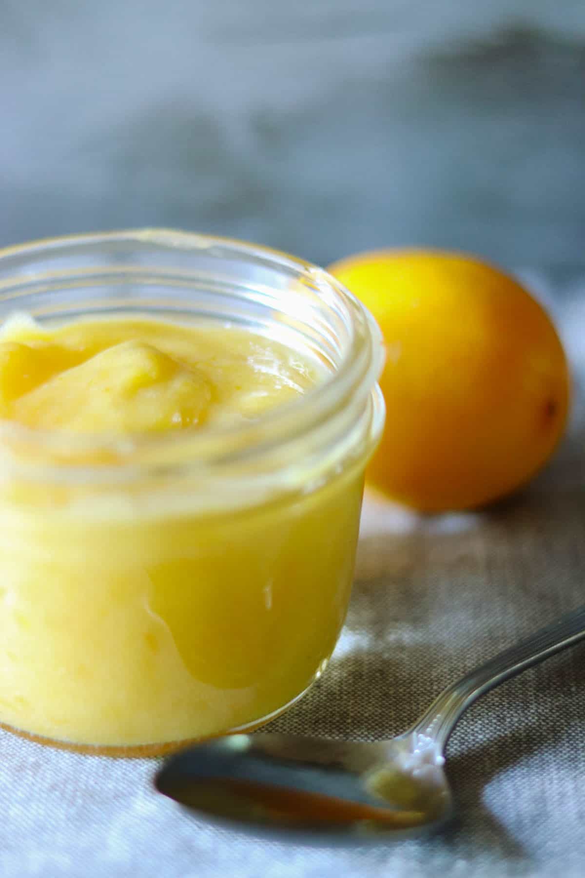 Lemon Curd in a jar next to a spoon.