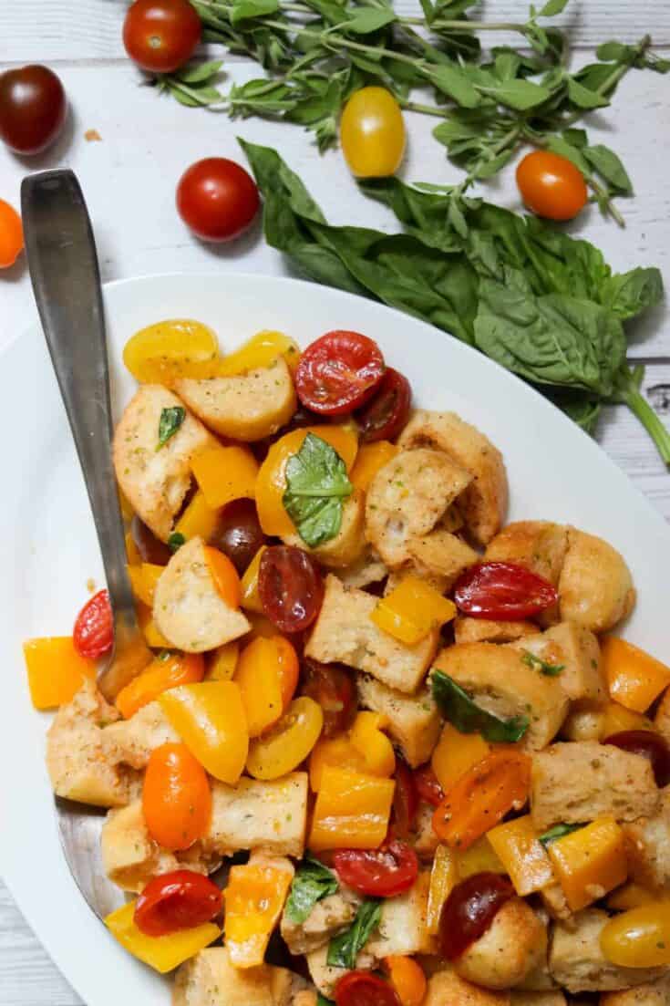 Panzanella salad with a large spoon and fresh herbs.