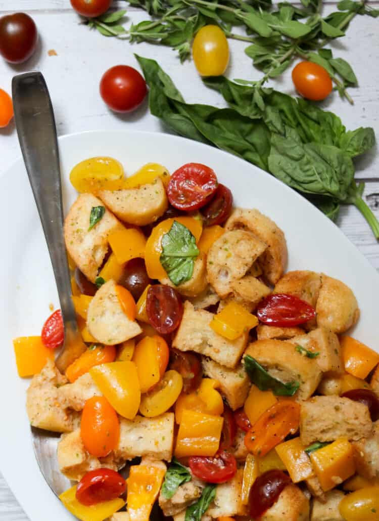 Panzanella salad with a large spoon and fresh herbs.