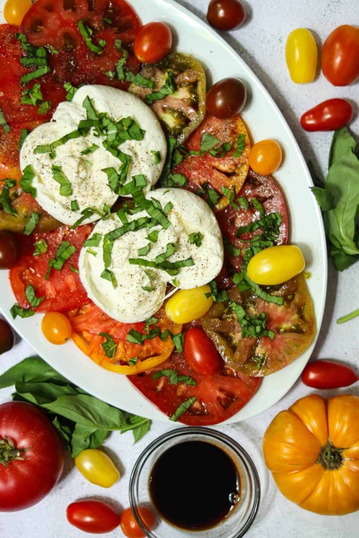 photo of a burrata caprese salad with a dish of balsamic vinegar and fresh basil leaves.