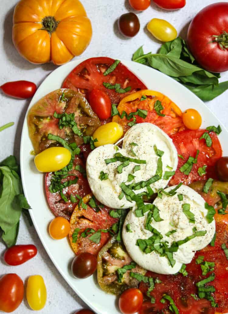photo of caprese salad with burrata cheese on a white plate.