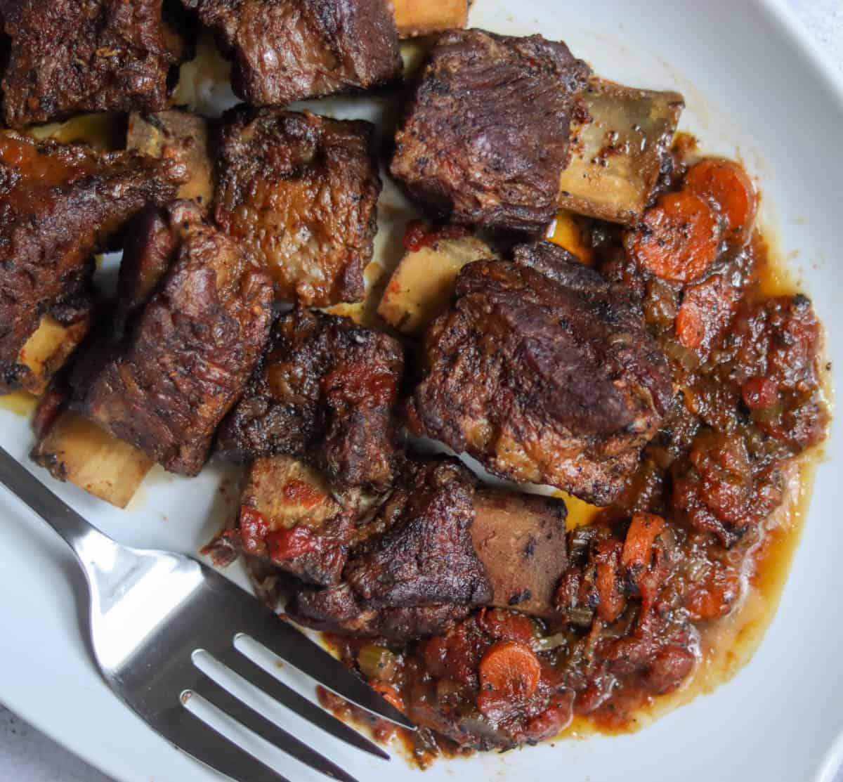 close up photo of short ribs on a white plate with a serving fork.