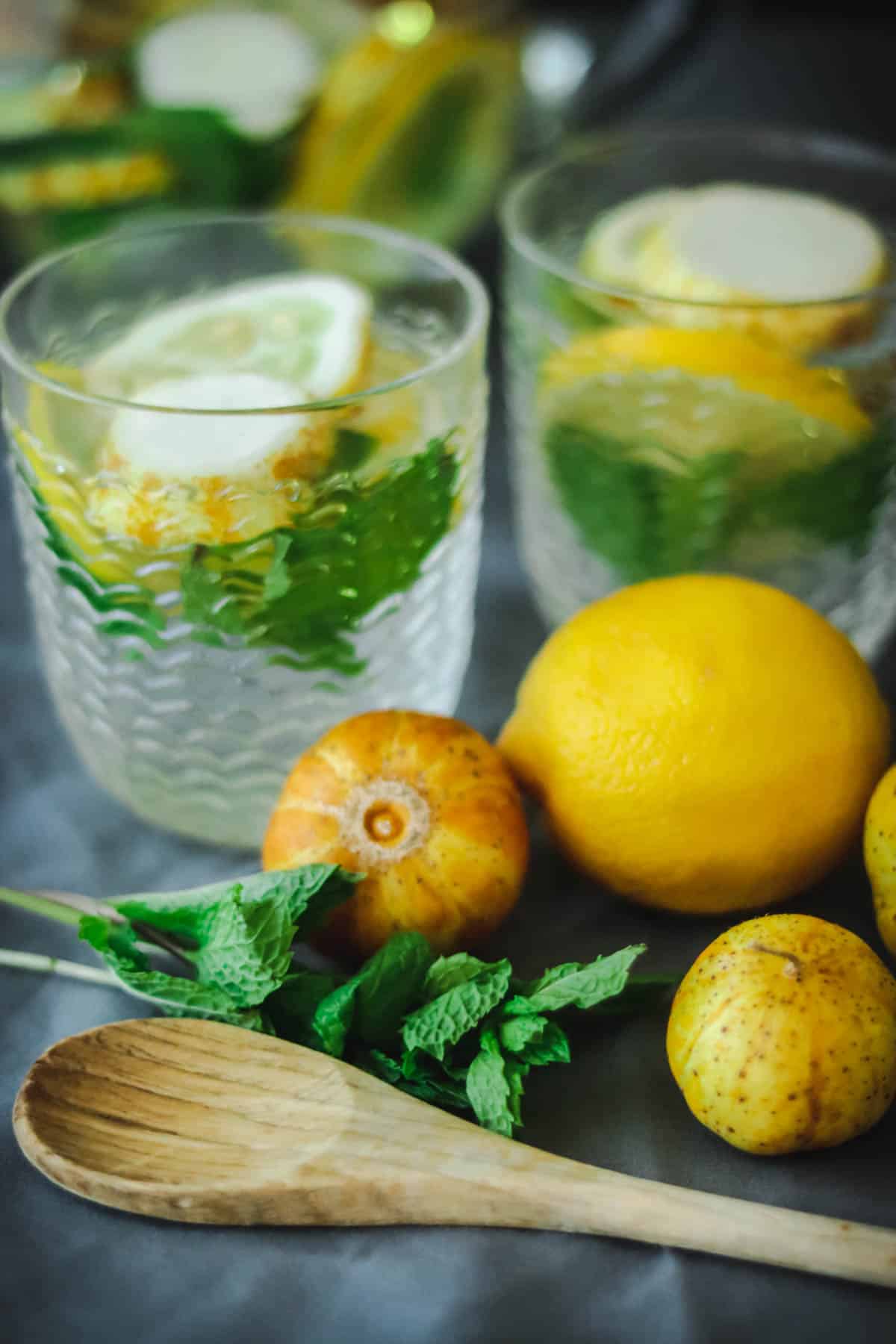 Glasses of lemon cucumber water with mint leaves and a wooden spoon.