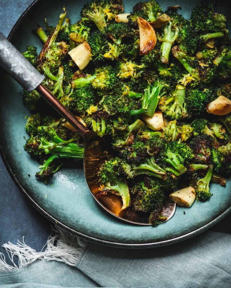 Charred roasted broccoli in a bowl with a spoon and napkin.
