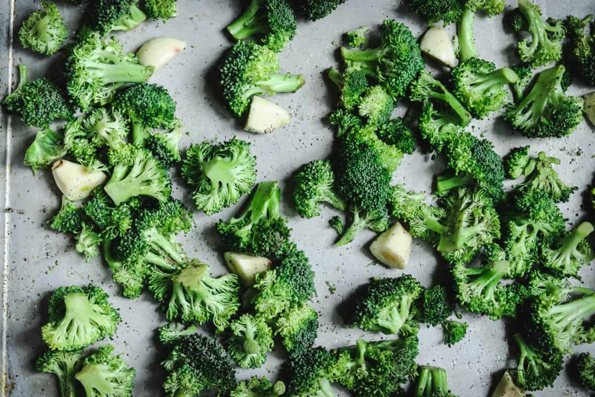 Seasoned broccoli and garlic cloves on a sheet pan.