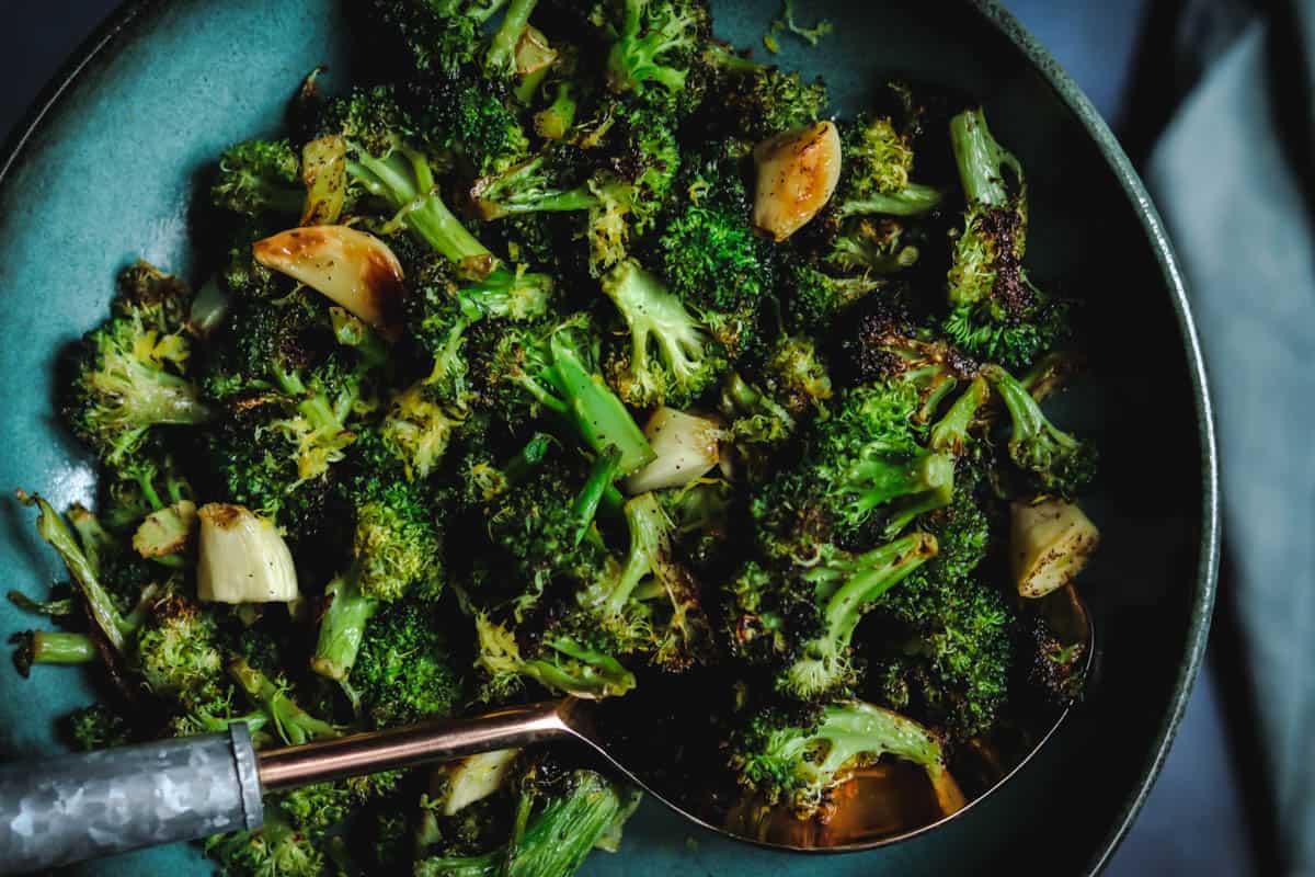 charred broccoli in a green bowl with a metal spoon.