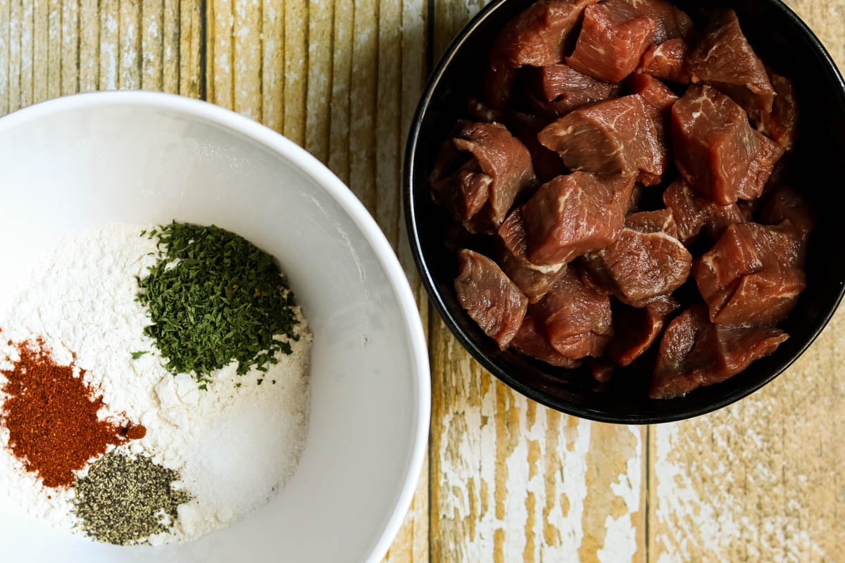 Beef stew meat and flour with seasonings in two bowls.