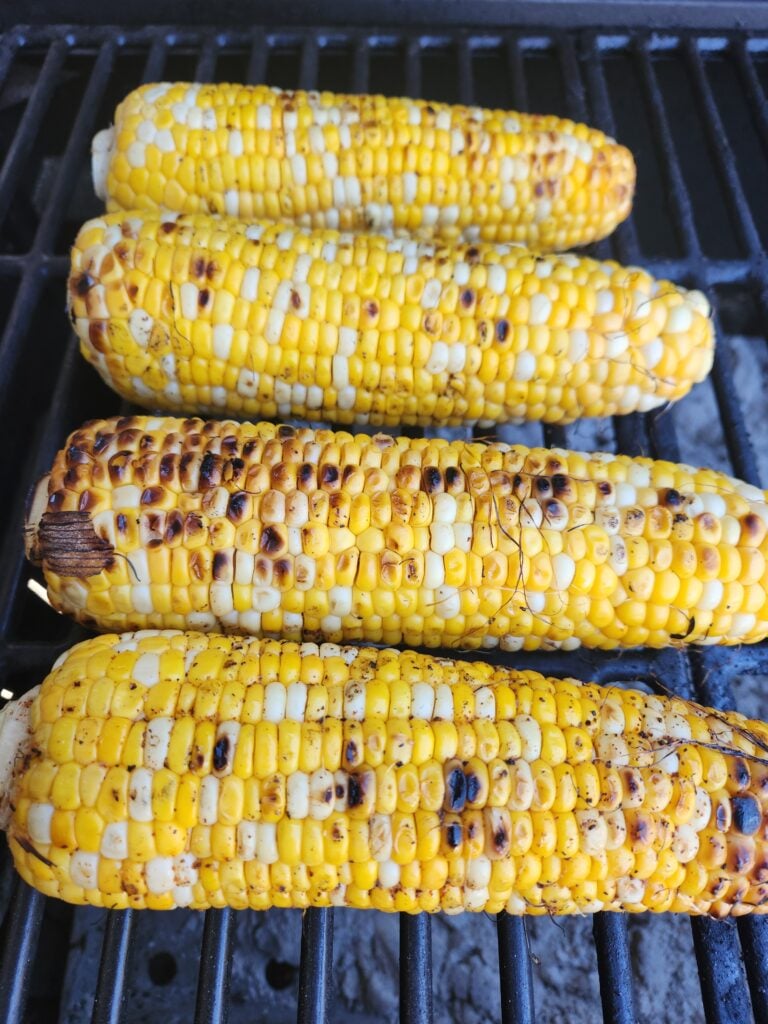 Four ears of corn on a charcoal grill.
