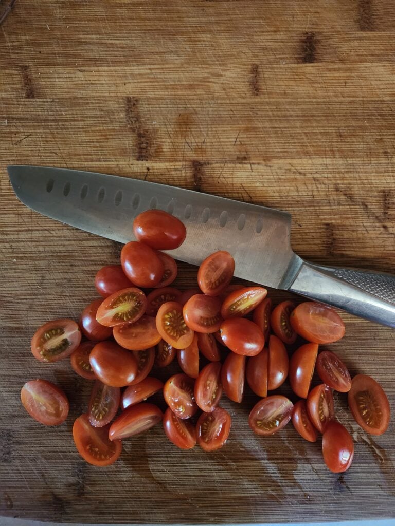Cherry tomatoes on a wooden cutting board with a knife.