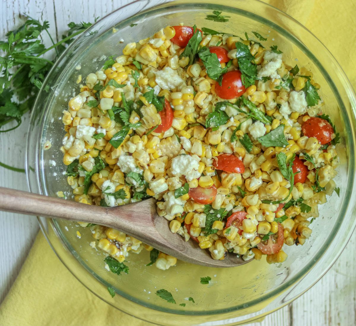 Bowl of fresh grilled corn salad and a wooden spoon.