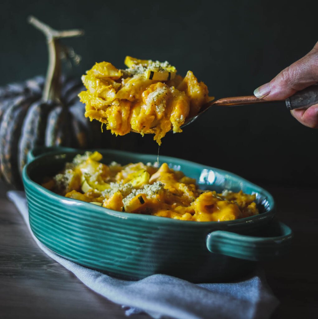 Squash mac and cheese on a spoon above a green casserole dish.