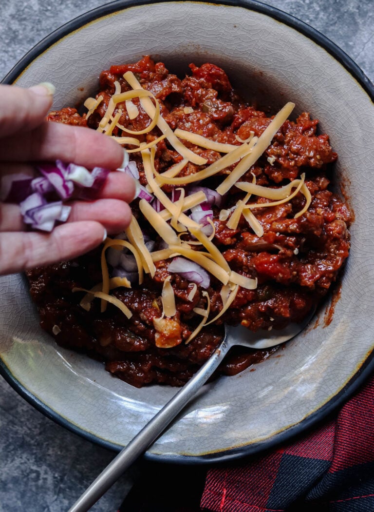 Adding chopped raw onion to a bowl of no bean chili.