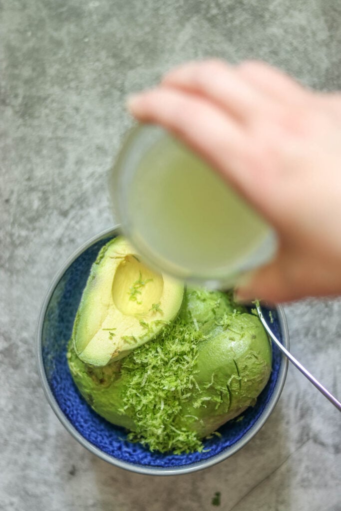 Pouring lime juice on the avocado halves.