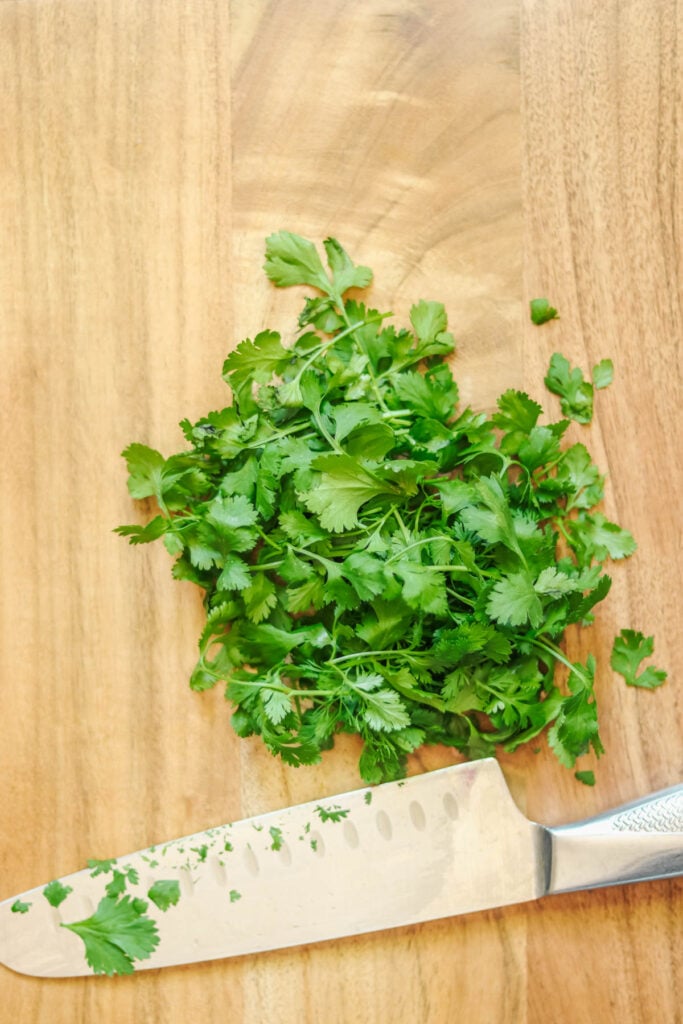Cilantro and a knife on a cutting board.