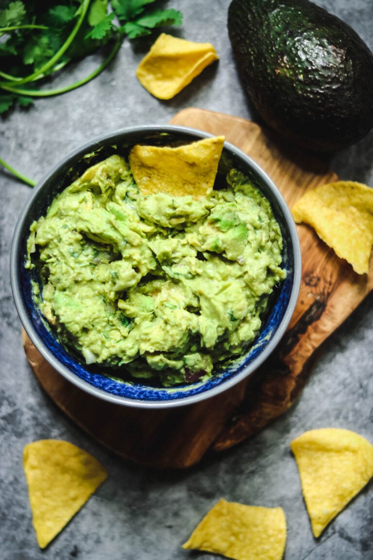 Guacamole in a blue bowl with tortilla chips on a gray background.