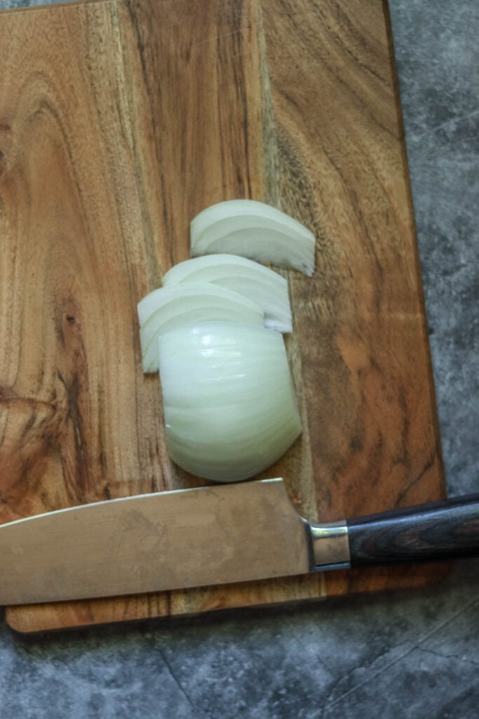 Onion cut into wedges next to a knife.