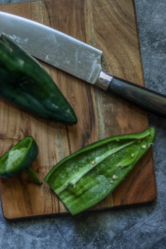 Poblanos cut in half on a wooden cutting board.