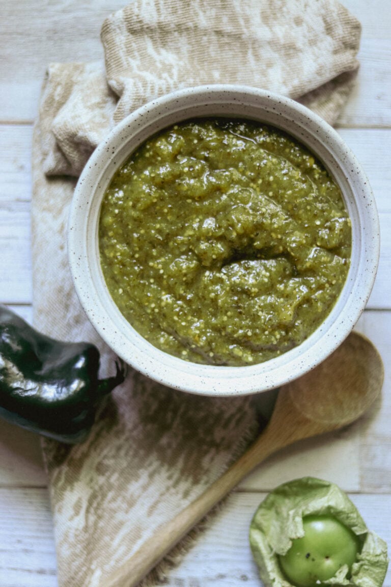 Salsa verde in a white stoneware bowl with a wooden spoon.