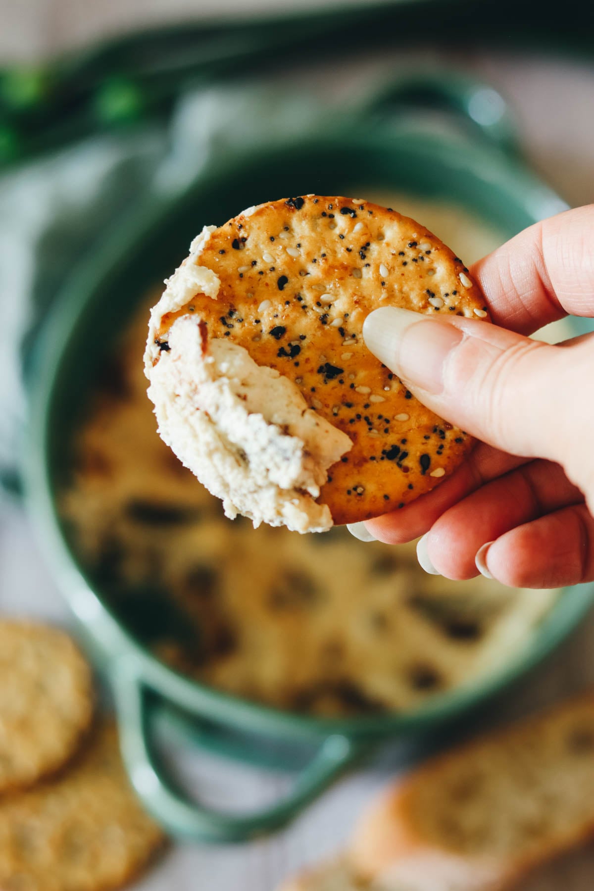 Amy's hand holding a cracker with bacon dip.