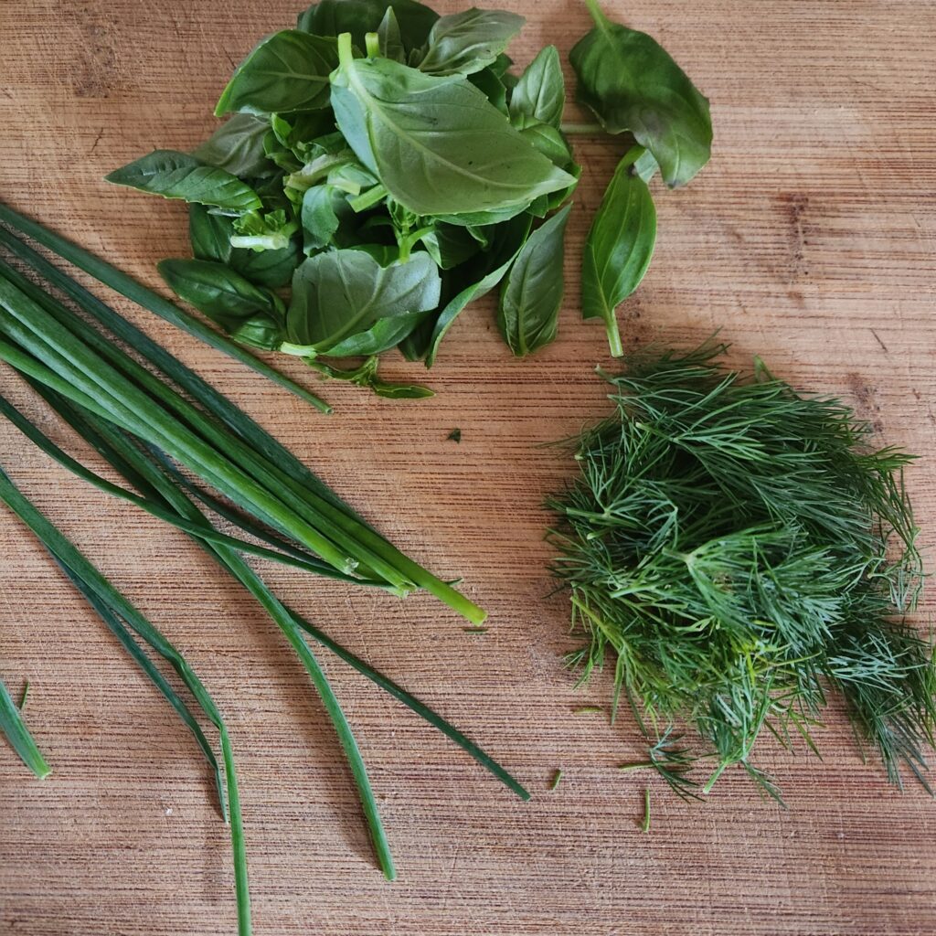 Fresh basil, dill, and chives on a cutting board.
