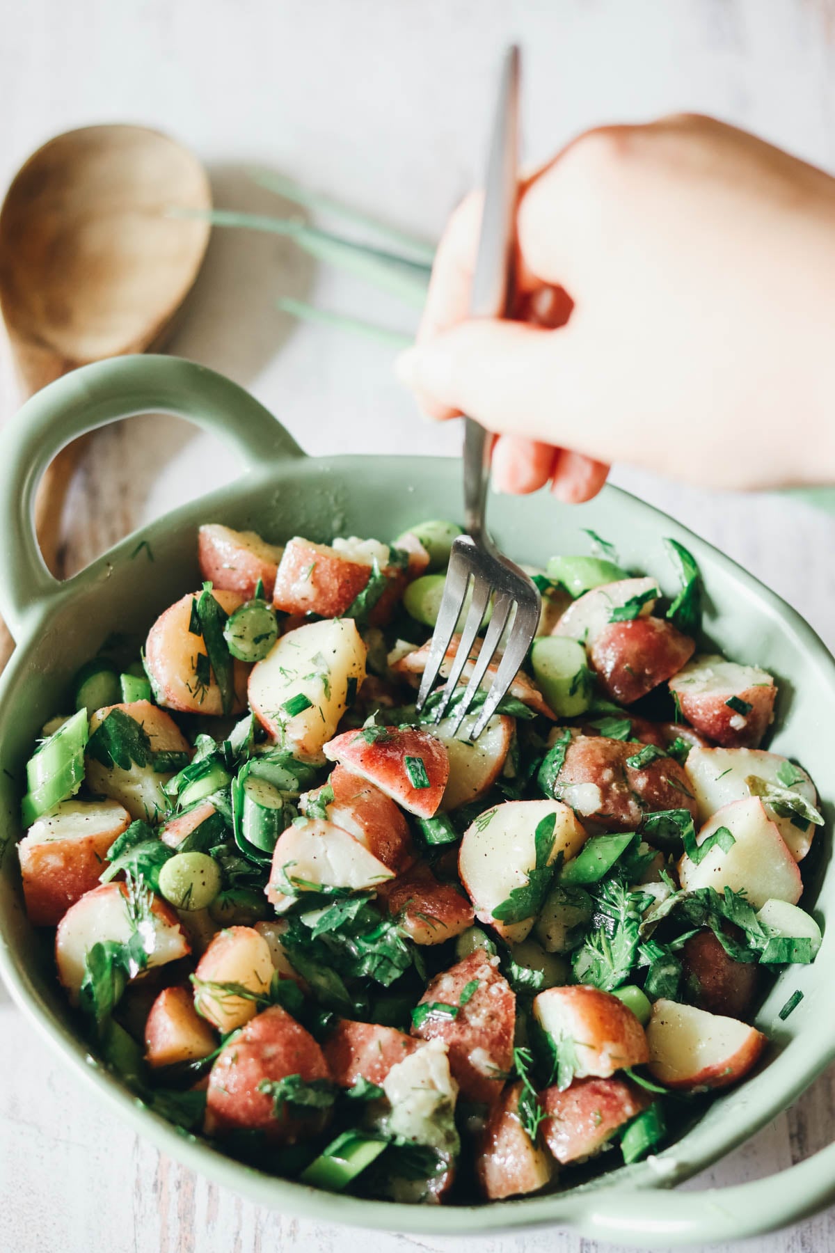 Amy's hand holding a fork over a bowl of potato salad.